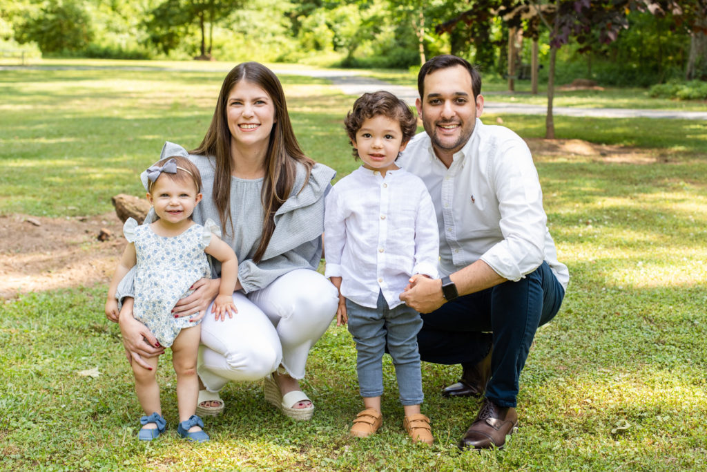 parents kneeling and toddlers legit toddlers standing and smiling mom wearing gray top and white pant toddler girl gearing a white and blue jumper Laure Photography
