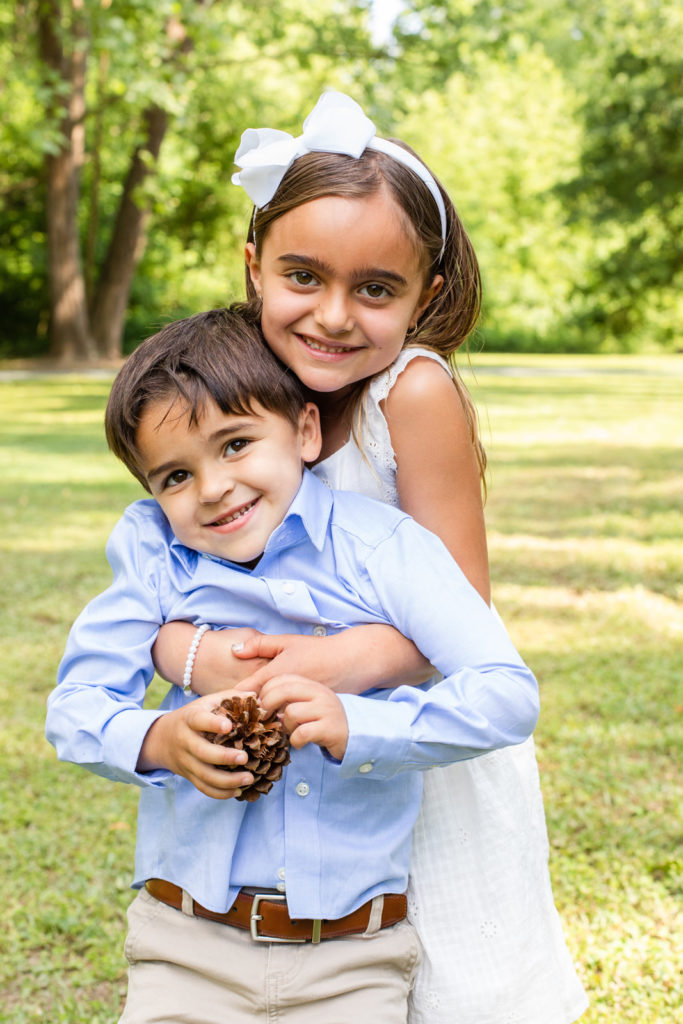 siblings boy and girl hugging in an Atlanta park during family photo shoot with photographer Laure Photography both wearing coordinated outfits to toddlers size all wearing coordinated white and blue outfits during Spring extended family photo session with Laure Photography i Sandy Spring GA