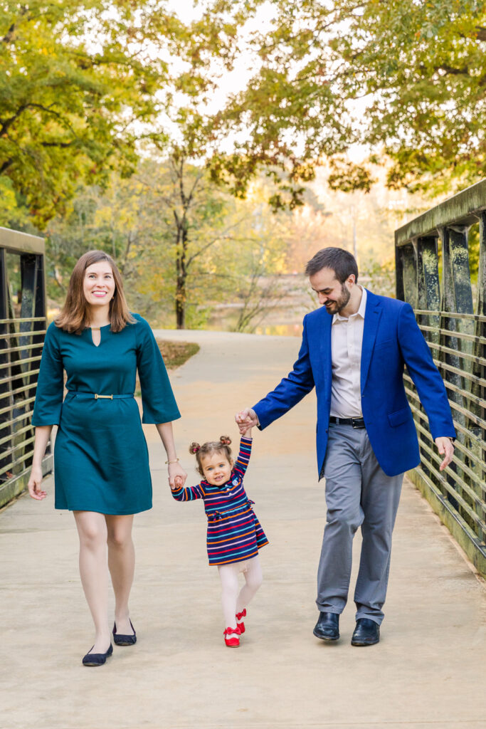 Lifestyle picture family with toddler daughter walking holding hands on a bridge