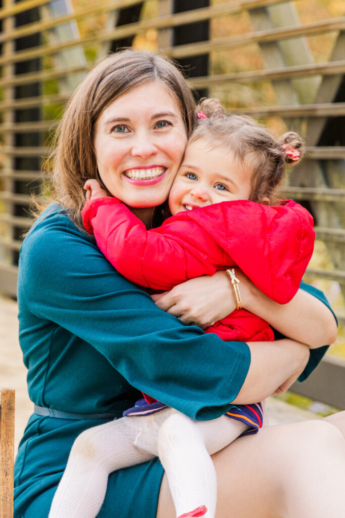 mommy wearing green dress hugging toddler daughter wearing red coat in an Atlanta park