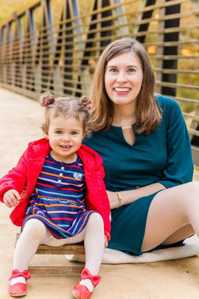 mom sitting on a blanket next to her toddler daughter sitting on a baby chair on a bridge in an Atlanta park