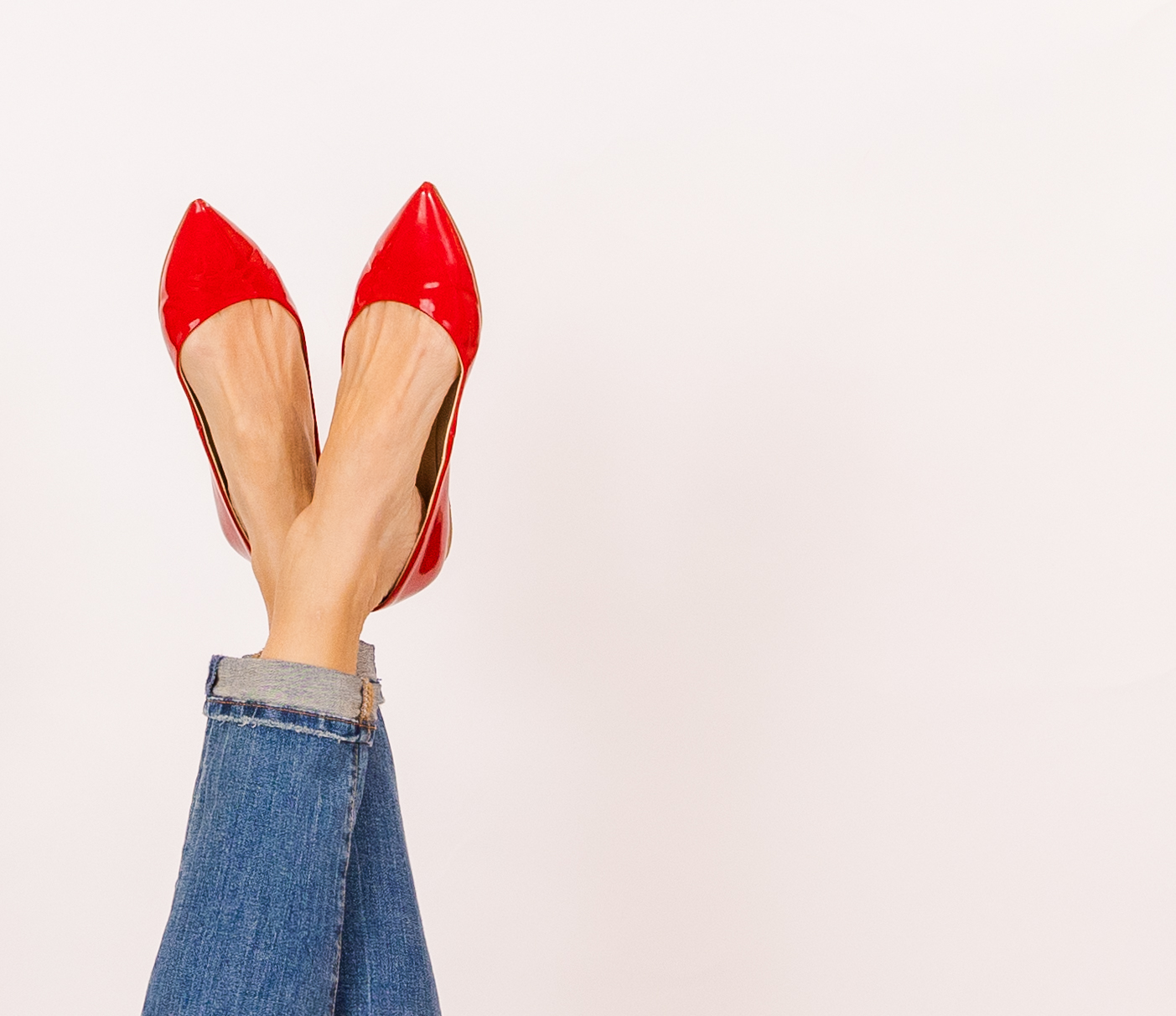 women's legs with jeans and flat shinny red shoes on the left of the frame white negative space for overlay text on the right