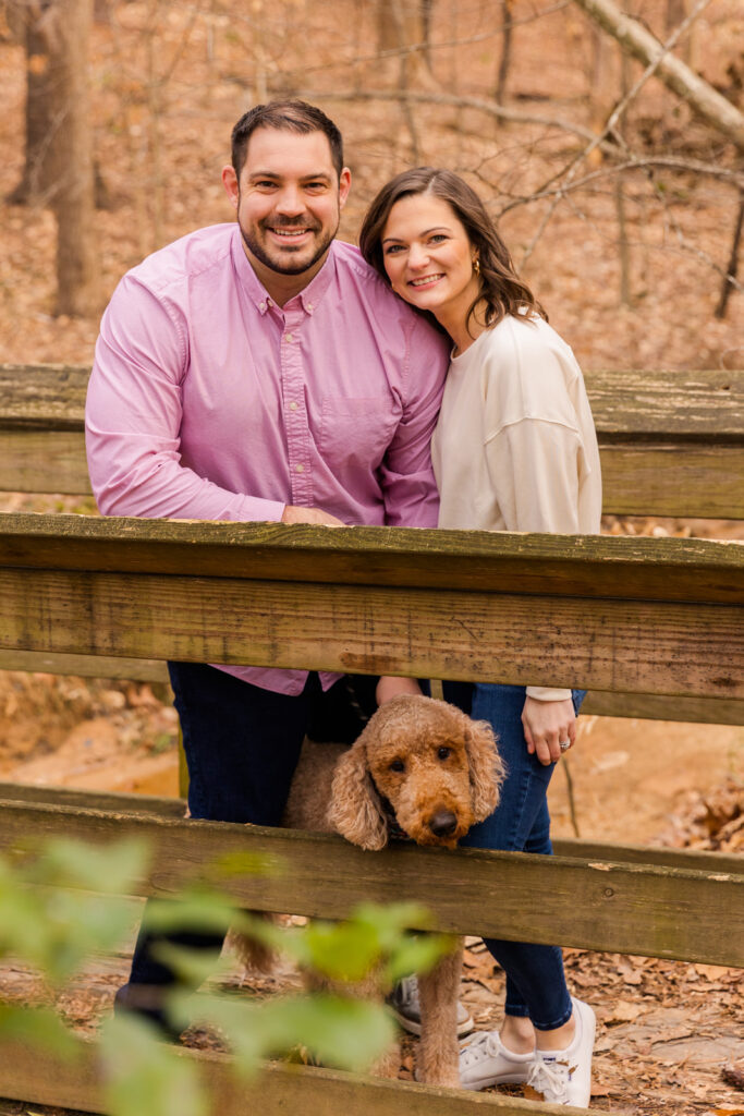 Couple with their dog standing on a wooden bridge in the woods during their photo session by Atlanta family photographer Laure Photography