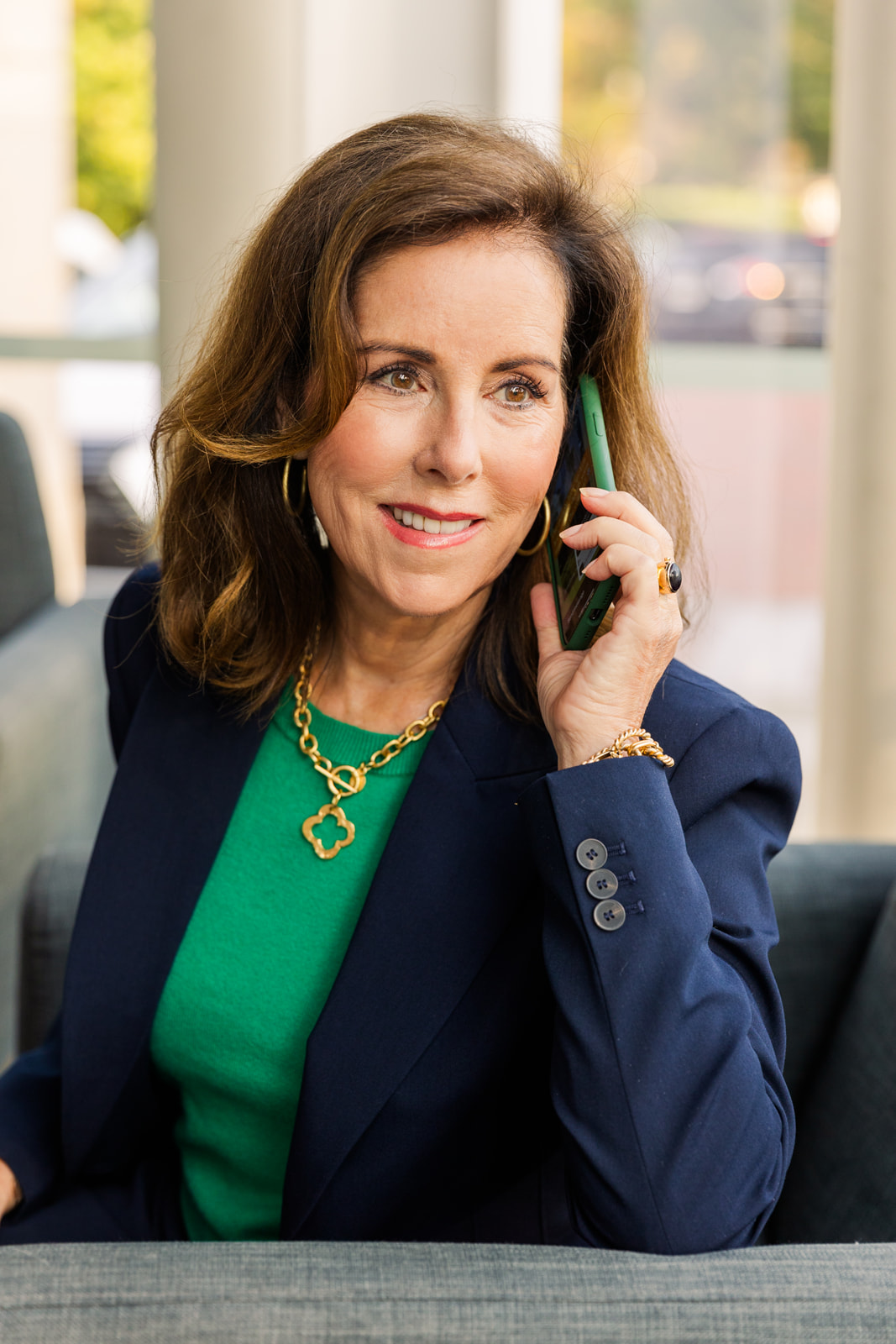 woman wearing a green top and navy blue jacket sitting on an armchair and talking on the phone during brand photo shoot Atlanta with Laure Photography