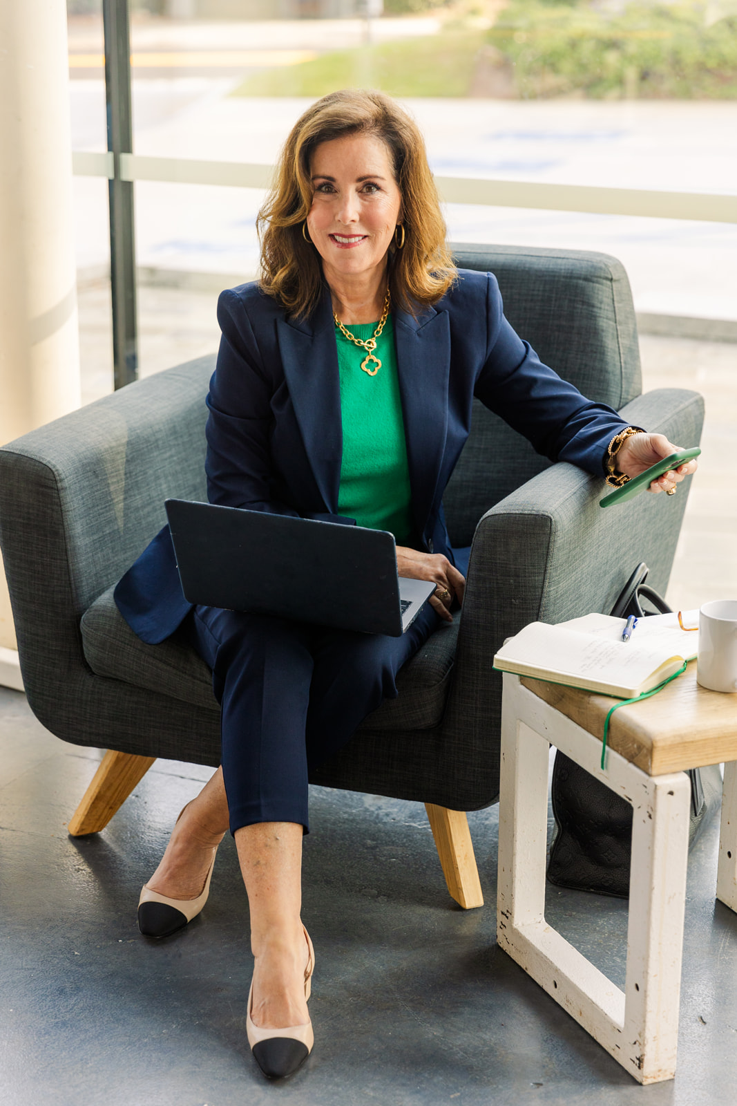 woman wearing a green top and navy blue jacket sitting on an armchair and working on her computer during brand photo shoot Atlanta with Laure Photography