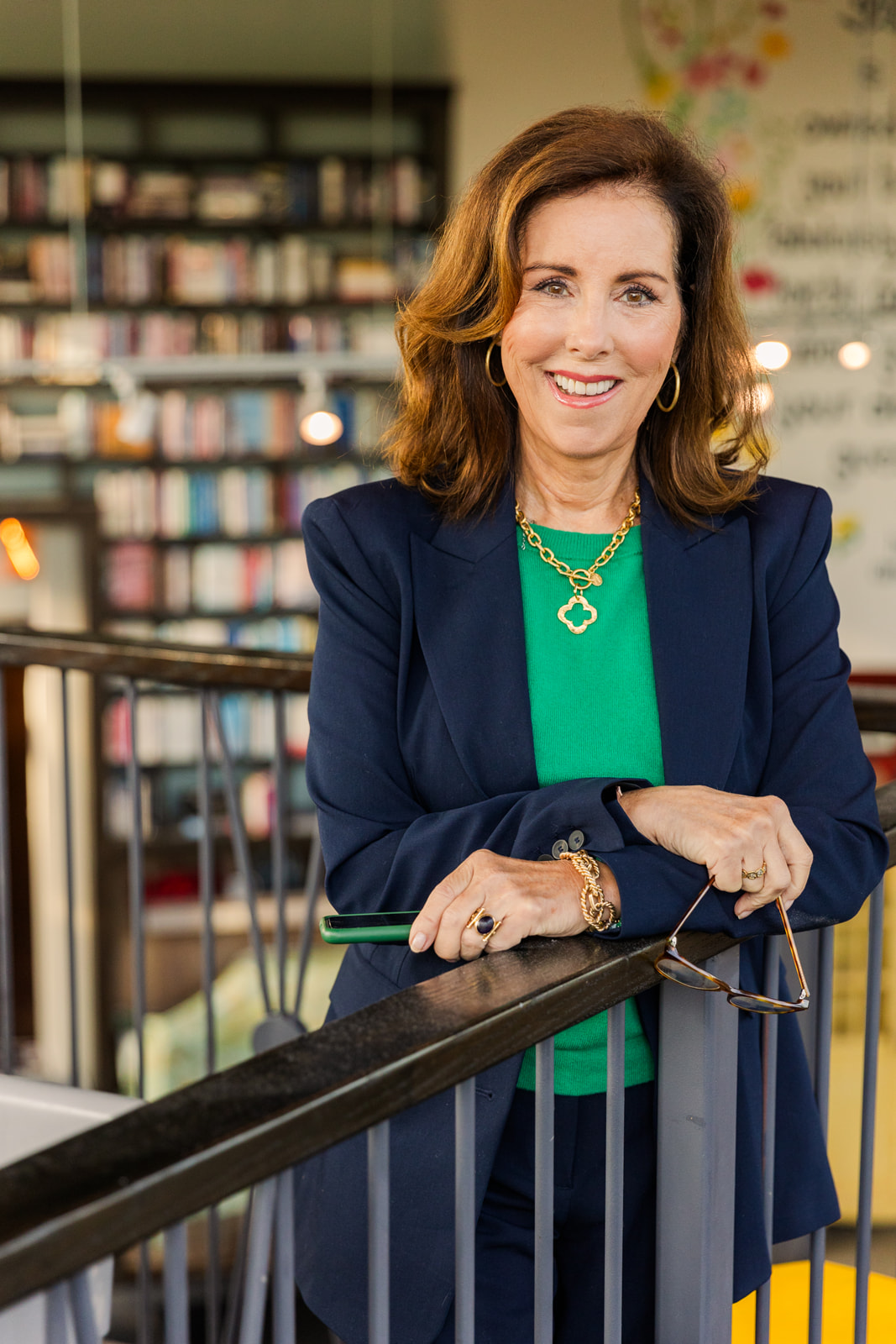 woman wearing a green top and navy blue jacket standing in front of book shelves and smiling at the camera during brand photo shoot Atlanta with Laure Photography