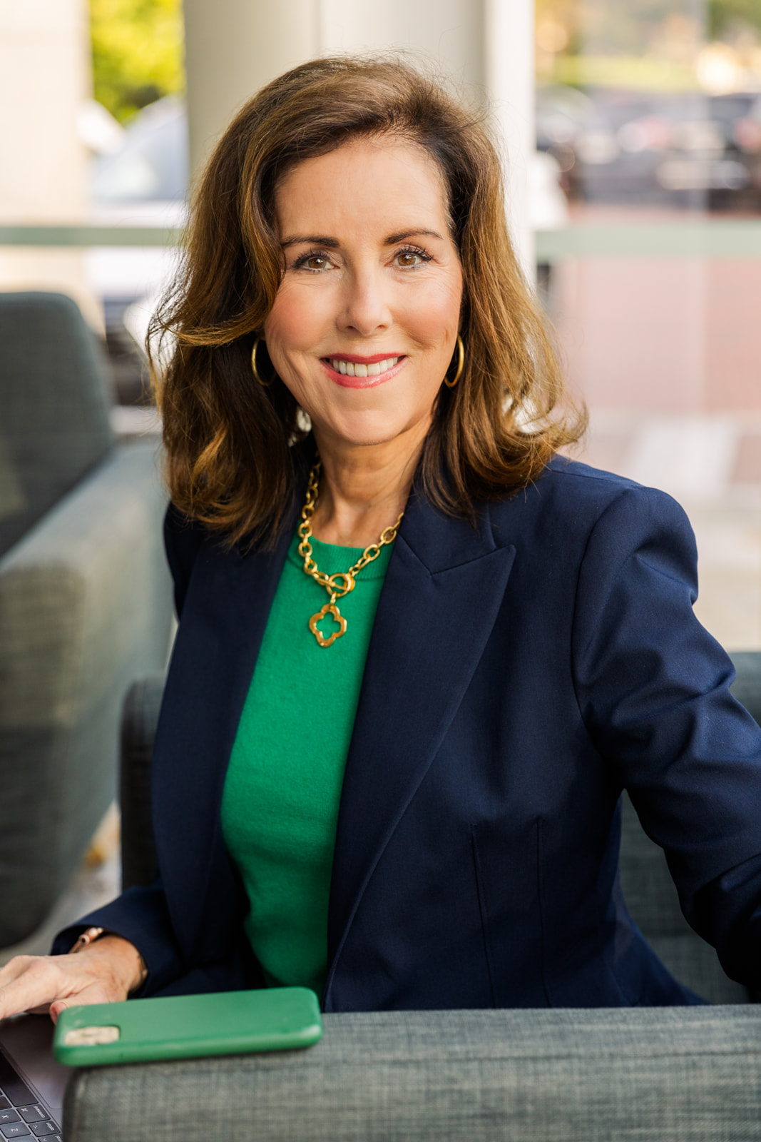 woman wearing a green top and navy blue jacket sitting on an armchair and smiling at the camera during brand photo shoot Atlanta with Laure Photography