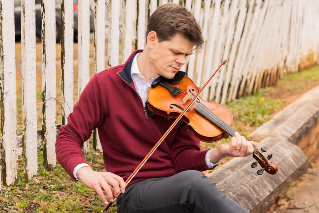 Consultant playing the violin in business casual attire near a fence during a brand session in Atlanta, by Laure Photography