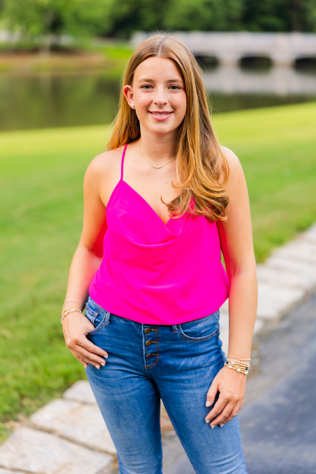 teenager girl standing on a path in front of a pond and a bridge in Lenox park during senior photoshoot