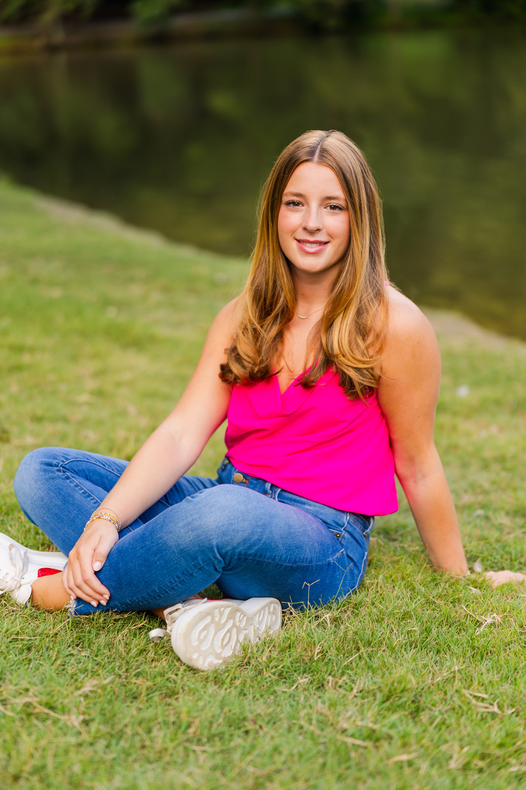 teenager sitting criss cross on the grass in front of a pond in Buckhead during senior portraits