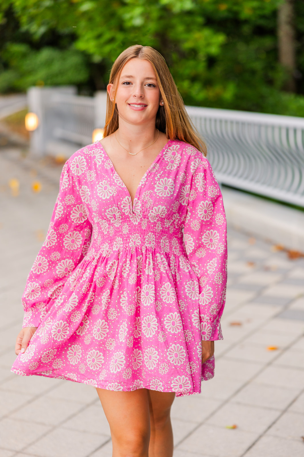 senior girl in fancy summer dress with long sleeves walking towards the camera hand holding the dress in Lenox Park during senior portraits