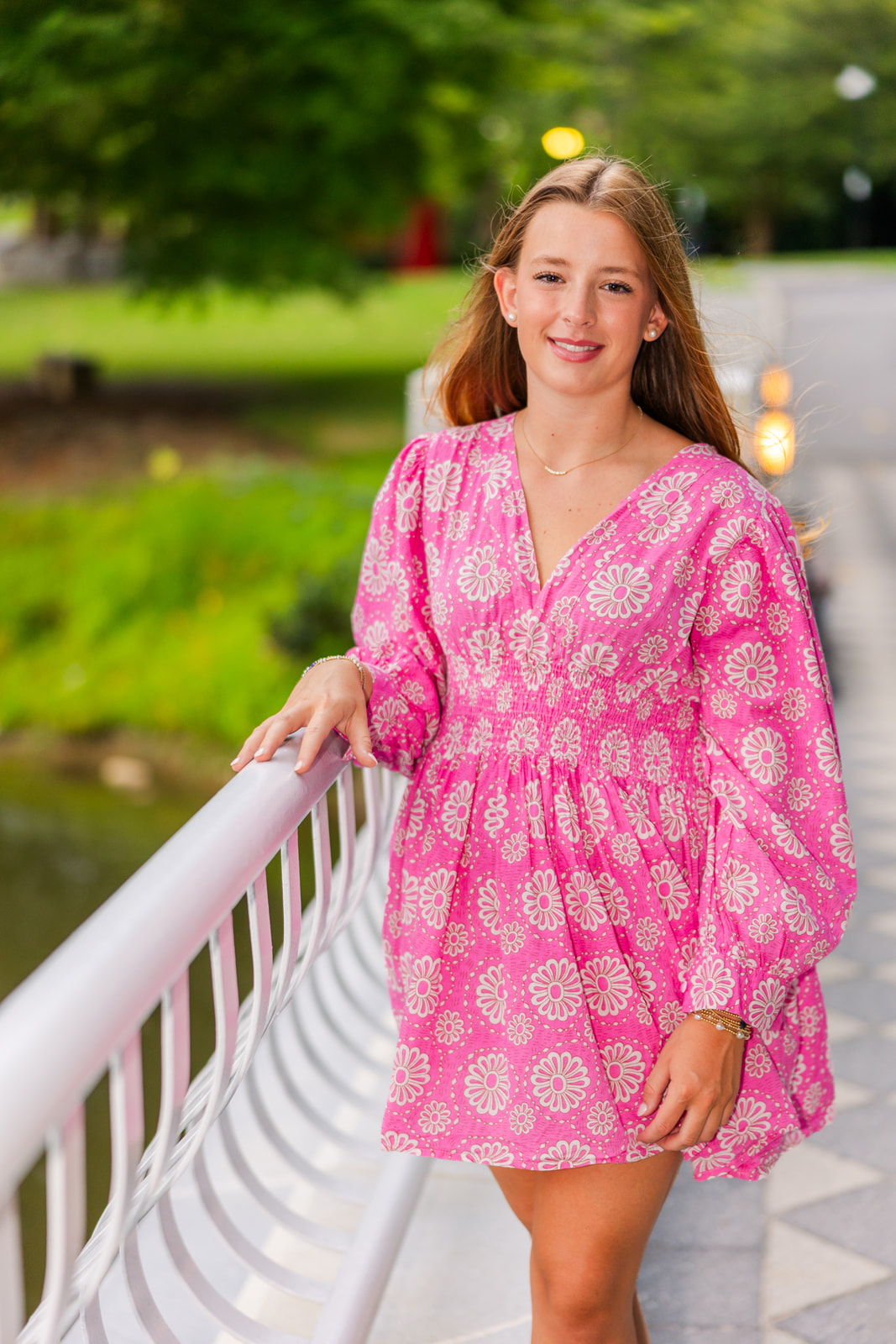 young adult girl wearing a short summer long sleeves pink and white dress standing on a bridge during portraits in Atlanta park