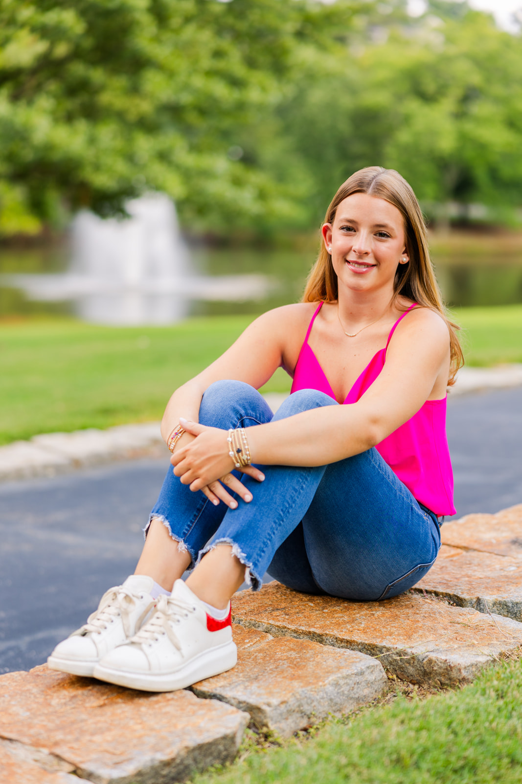 high school girl in jeans and colorful top sitting on the ground hugging her knees during senior photoshoot in Lenox Park Atlanta GA