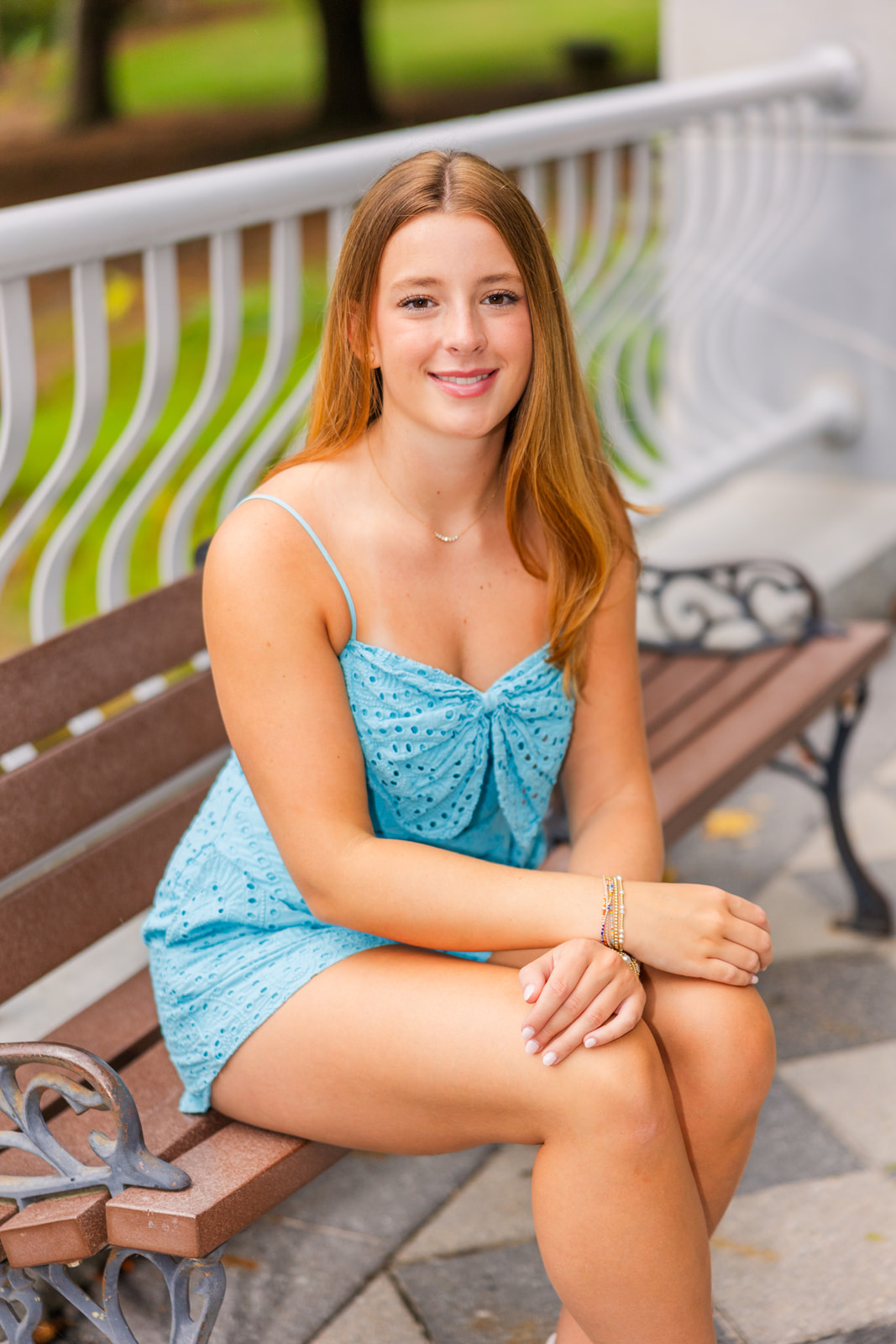 senior girl sitting on a bench on a bridge weary a light blue romper during her photo session in Atlanta Lenox Park