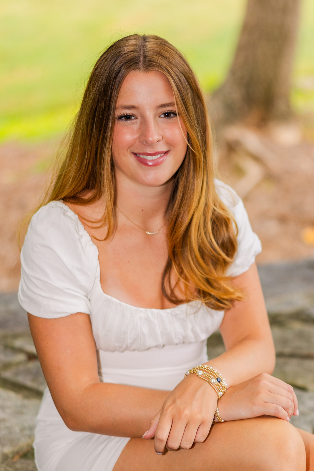 senior girl wearing a white dress sitting wristes crossed in Lenox Park during Senior portrait photo session