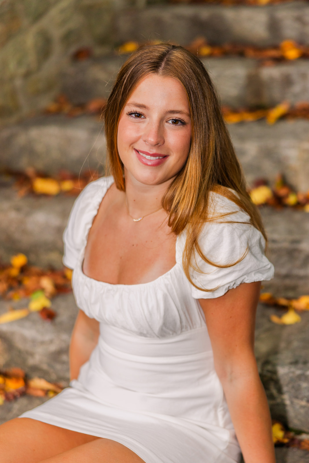 senior girl wearing a white summer dress sitting on stone stairs in an Atlanta Buckhead park during Senior portrait photo session