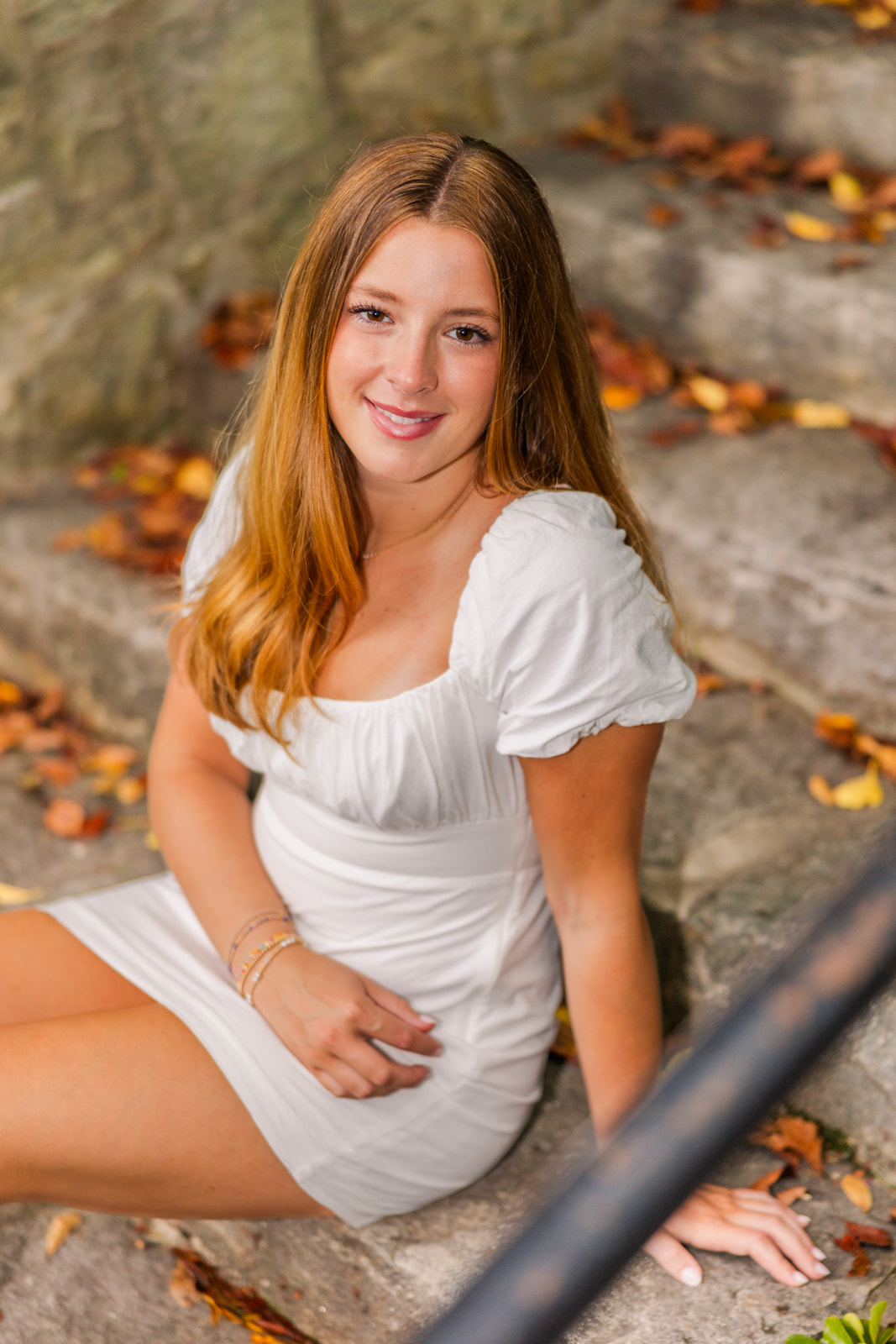 teenage girl wearing a white summer dress sitting on stone stairs in Lenox park Atlanta during Senior portrait photo session