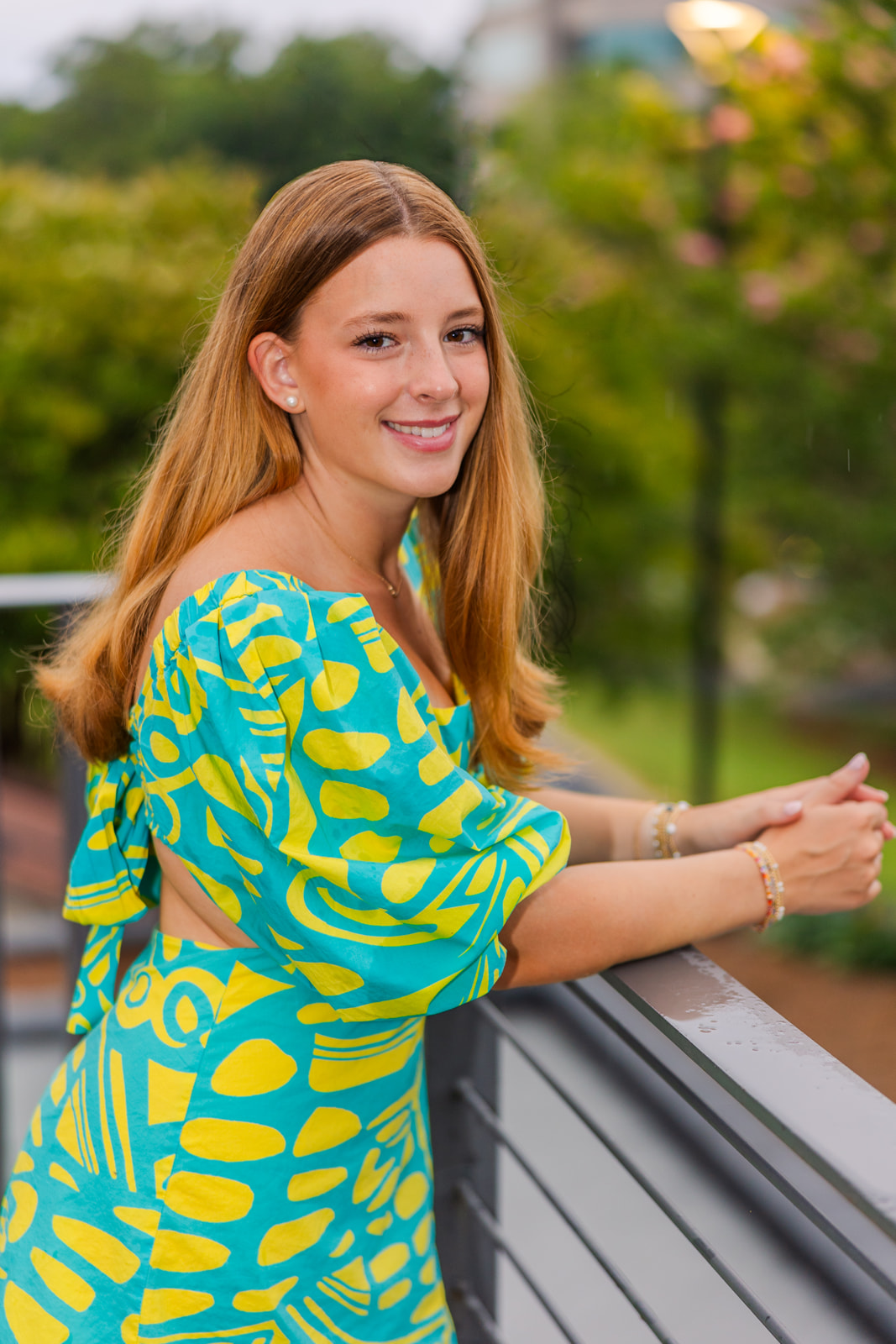 senior girl leaning on a ramp wearing colorful short dress with yellow patterns and a bow in the back looking at the camera sideway in Buckhead Park GA during portraits session