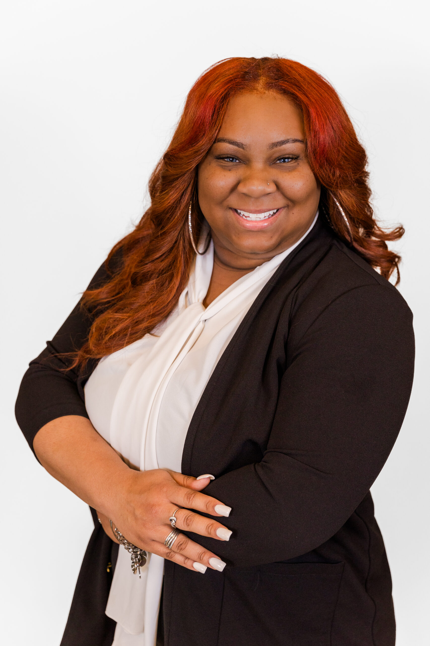 Ashley Ingram wearing white top and ball jacket arms crossed smiling at the camera in front of white backdrop during professional headshots organized at her office