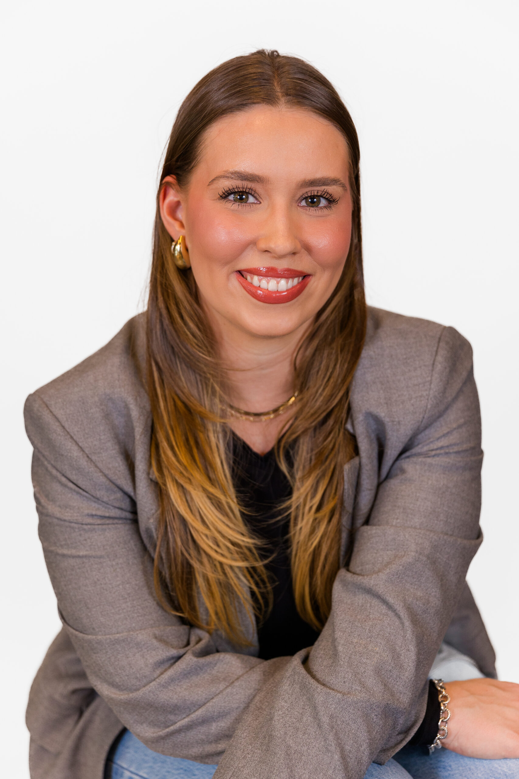 Ava Picken wearing a grey vest and sitting facing the camera in front of white backdrop during office headshot mini session