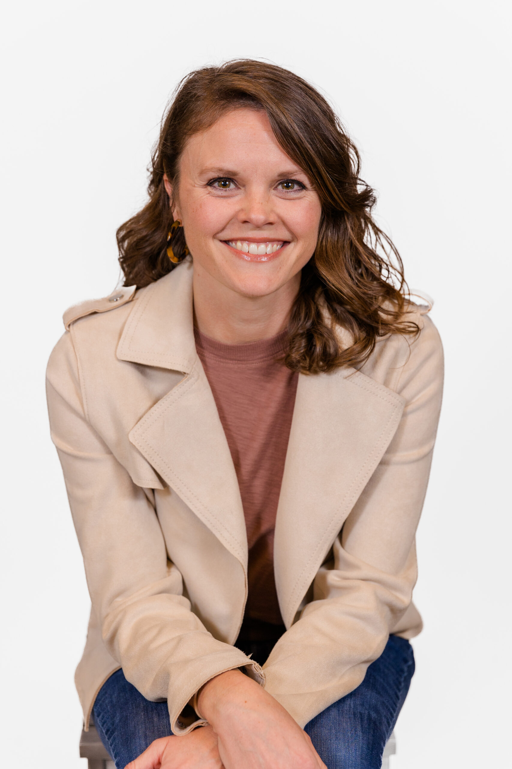 Woman Emily Philips sitting facing camera with beige jacket during professional headshots in front of white backdrop