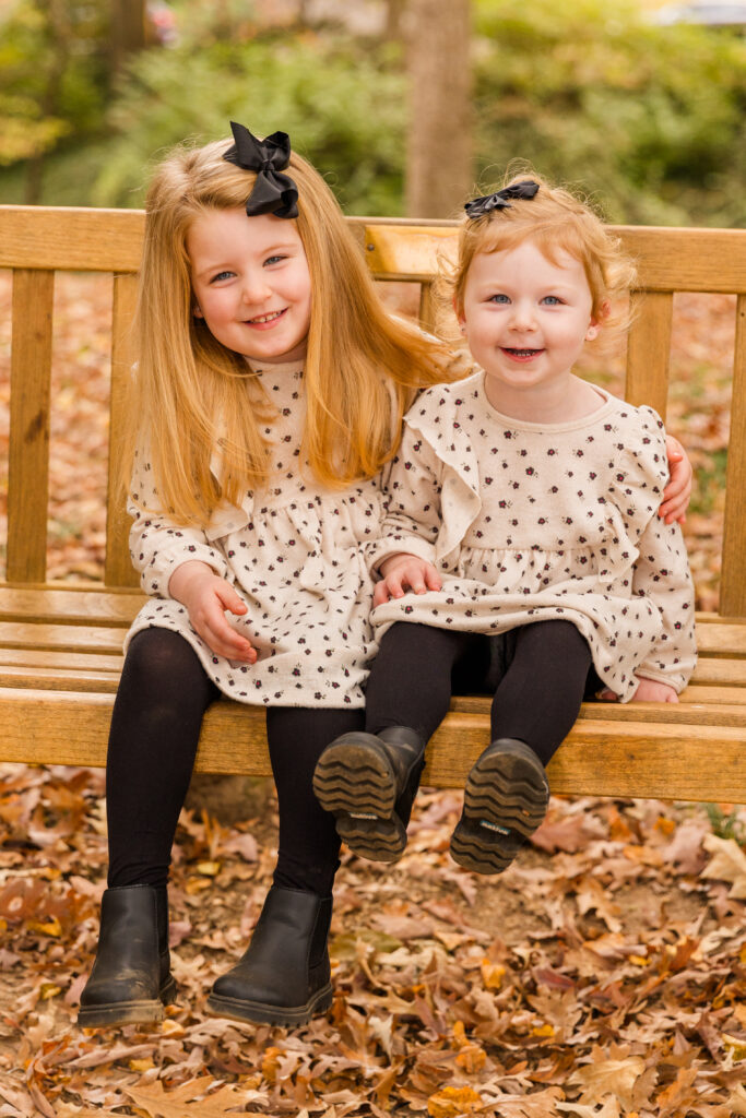 Young girl with sibling toddler sitting on a park bench and laughing