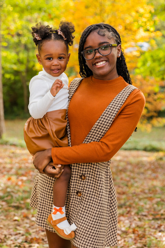 Teenager girl holding toddler sister wearing organic, white and brown outfit during a photo session in Atlanta park