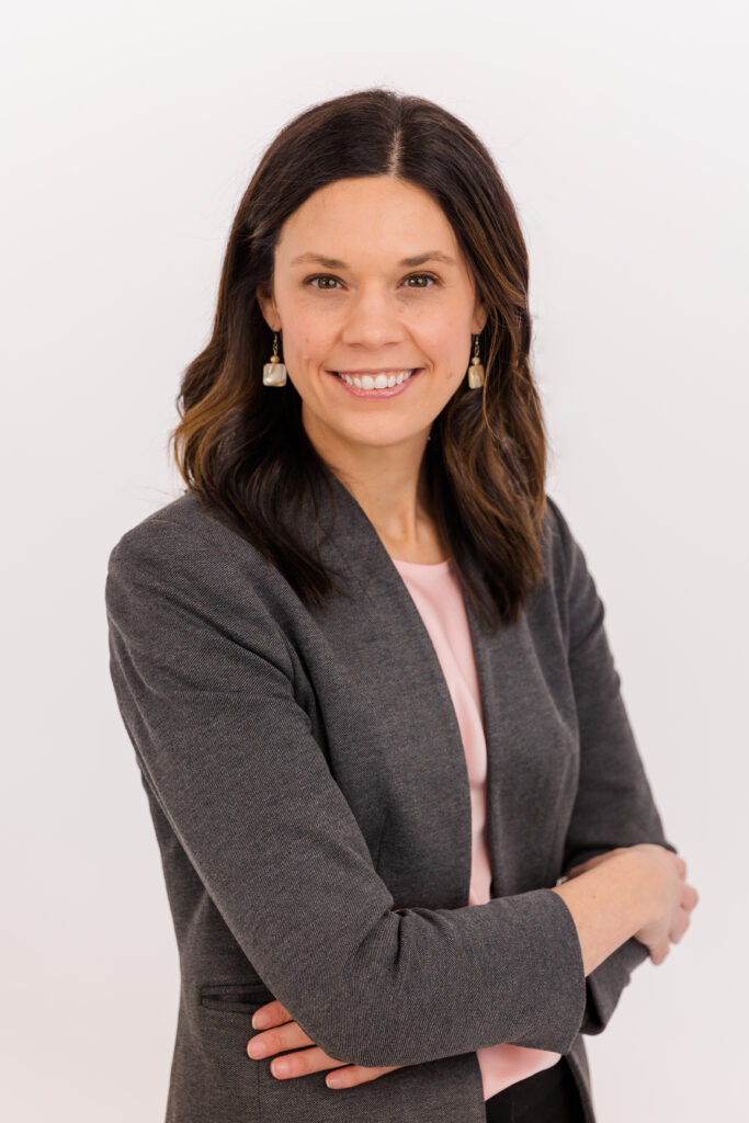 woman standing in front of white background arms crossed wearing corporate outfit light pink top and gray jacket during headshot photoshoot with Laure Photography