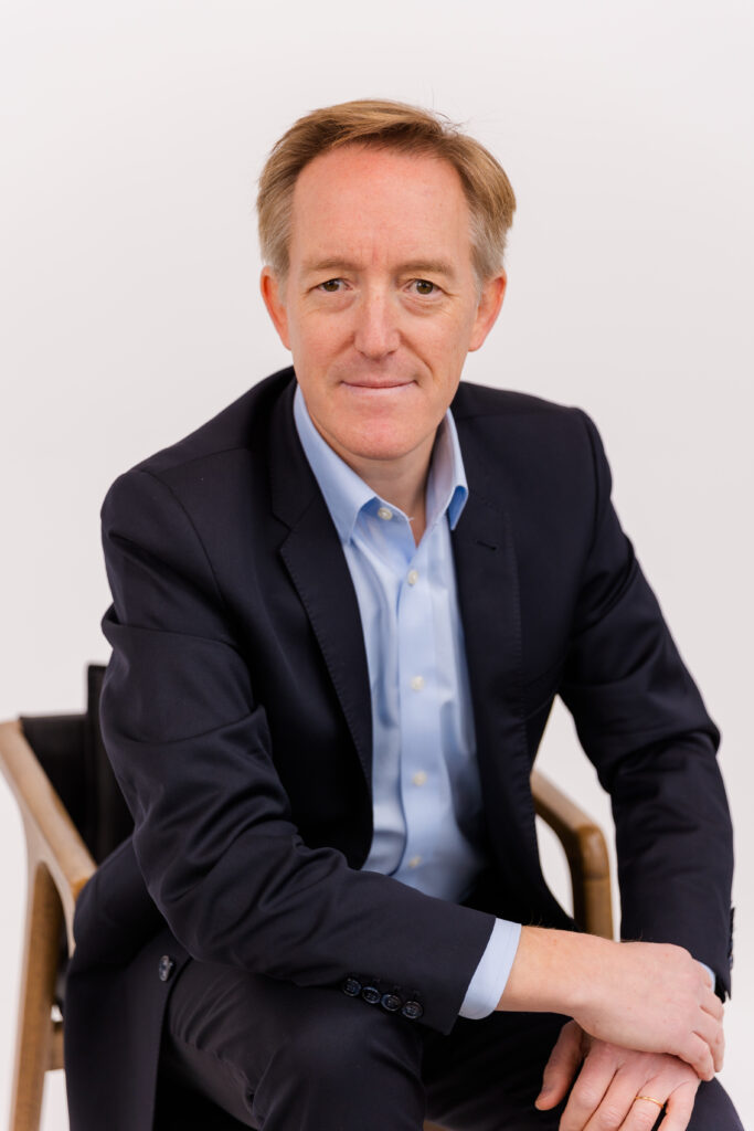 man sitting on a chair in front of white background wearing corporate outfit light blue shirt and dark jacket during headshot photoshoot with Laure Photography