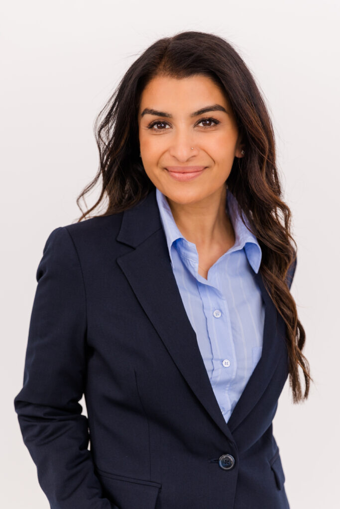 woman with long brown hair standing in front of white background wearing corporate outfit light blue shirt and dark blue jacket during headshot photoshoot with Laure Photography