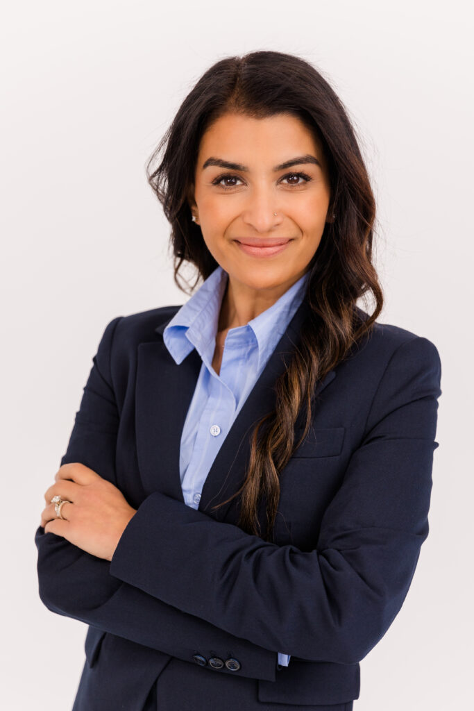 woman with long brown hair standing in front of white background arms crossed wearing corporate outfit light blue shirt and dark blue jacket during headshot photoshoot with Laure Photography