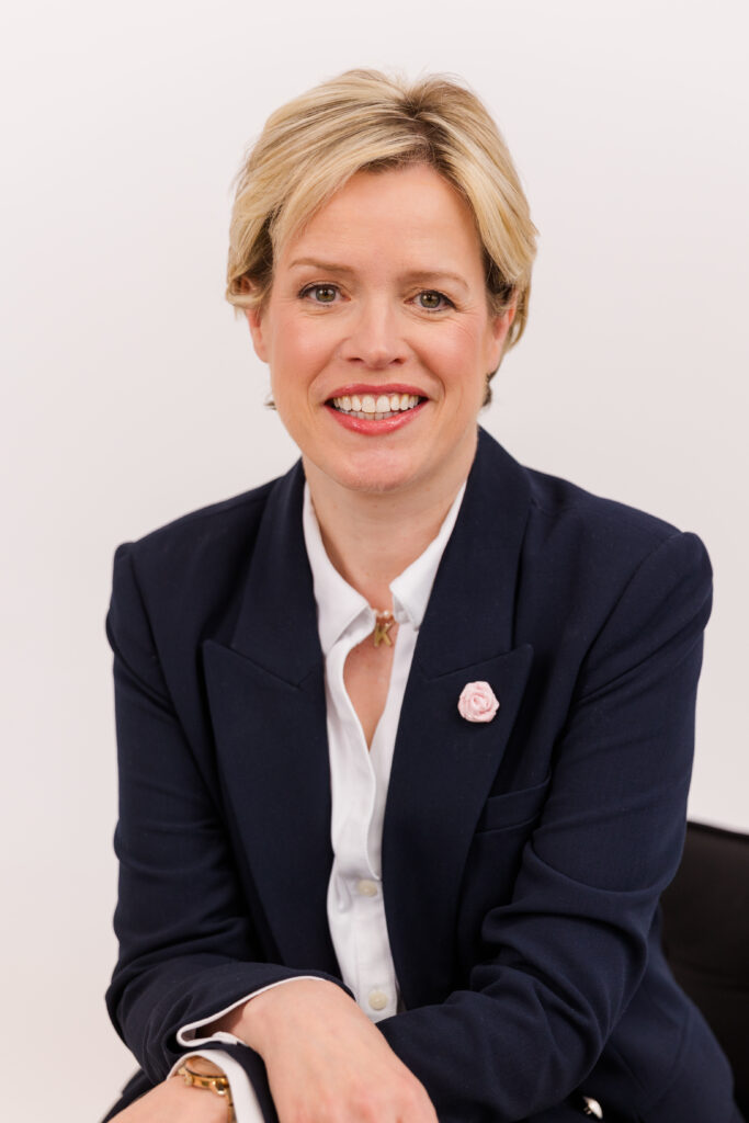 woman with short blonde hair sitting in front of white background wearing corporate outfit white shirt and dark blue jacket during headshot photoshoot with Laure Photography