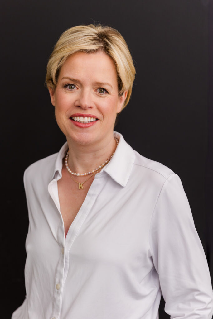 woman with short blonde hair standing in front of black background wearing corporate outfit white shirt during headshot photoshoot with Laure Photography
