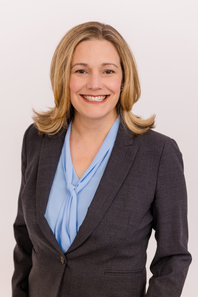 woman with blond hair standing. in front of white background wearing corporate outfit light blue top and gray jacket during headshot photoshoot with Laure Photography