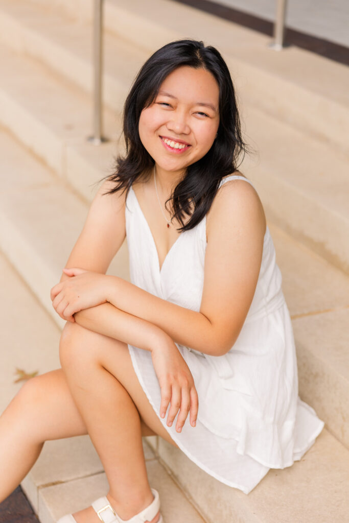 Senior girl in white sleeveless dress sitting on stairs during her Sandy Springs senior portraits with Laure Photography.