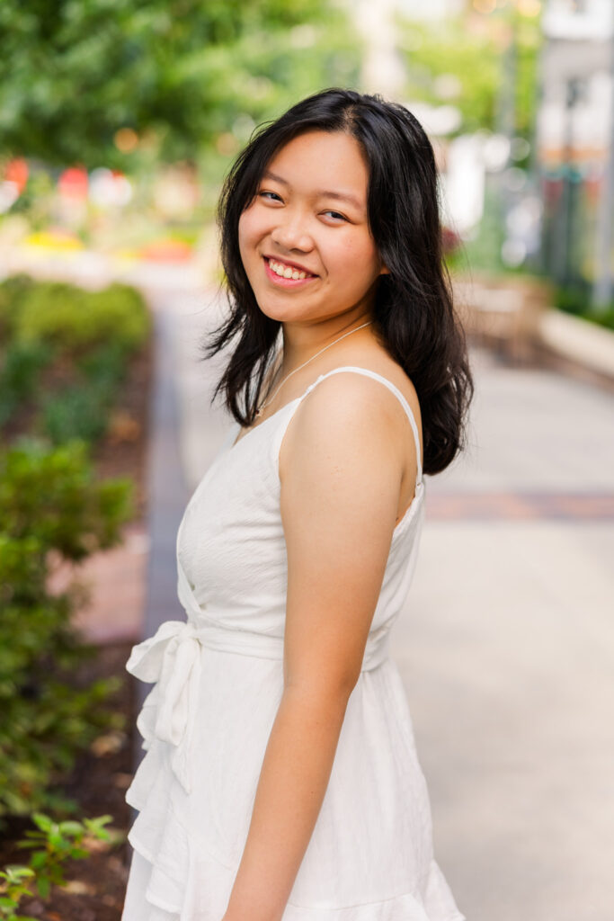 Senior girl in white dress standing on a city street, looking over her shoulder during Sandy Springs senior session with Laure Photography.