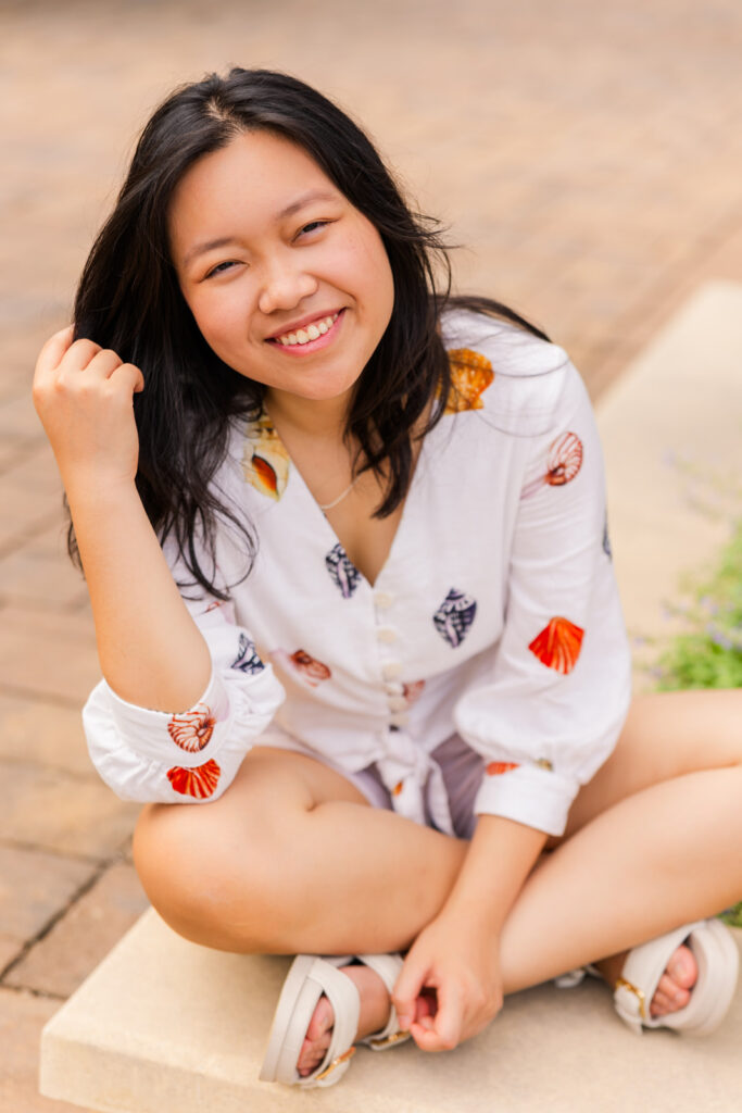 Senior girl sitting crisscross, hand in hair, facing the camera during her Sandy Springs senior photoshoot with Laure Photography.