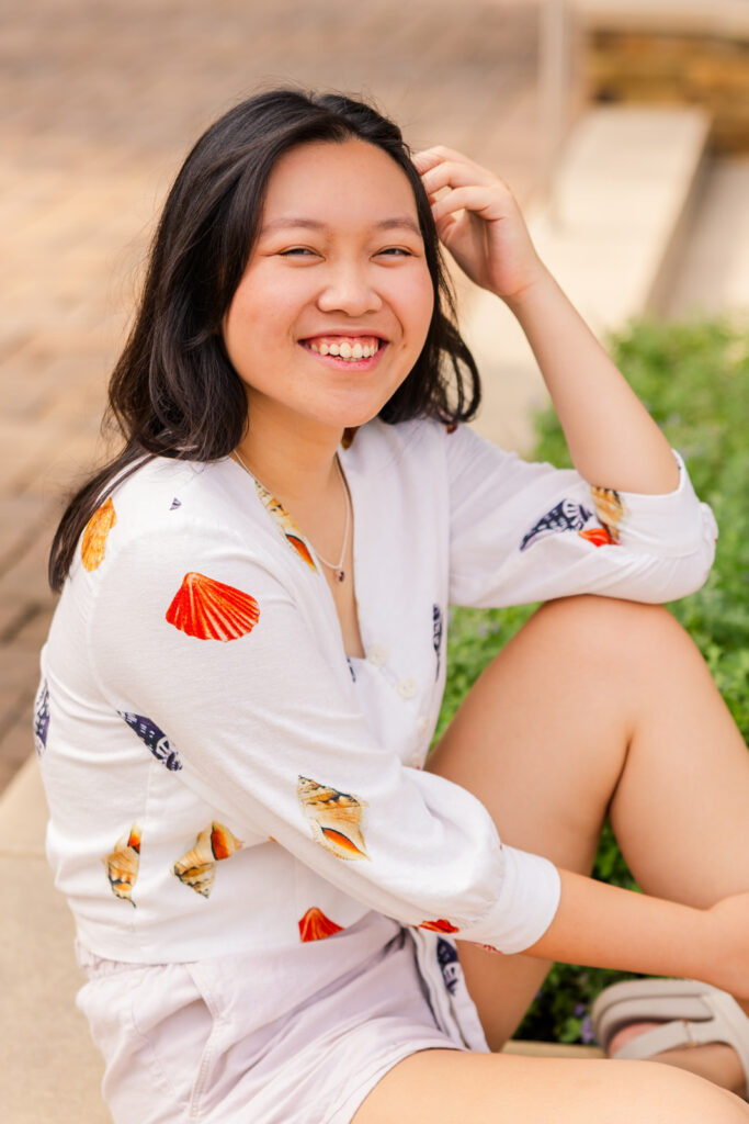 Senior girl sitting on the ground, hand in hair, gazing sideways during her Sandy Springs senior photoshoot with Laure Photography.