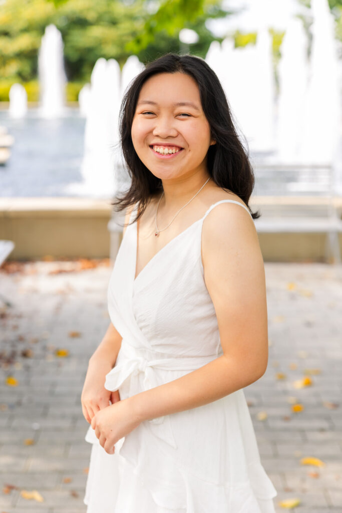 Senior girl in sleeveless white summer dress standing sideways with hands together during Atlanta senior portraits by Laure Photography.
