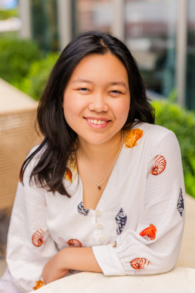 Senior girl sitting at a coffee shop table, elbow resting, wearing patterned shirt during her Sandy Springs senior portraits with Laure Photography.