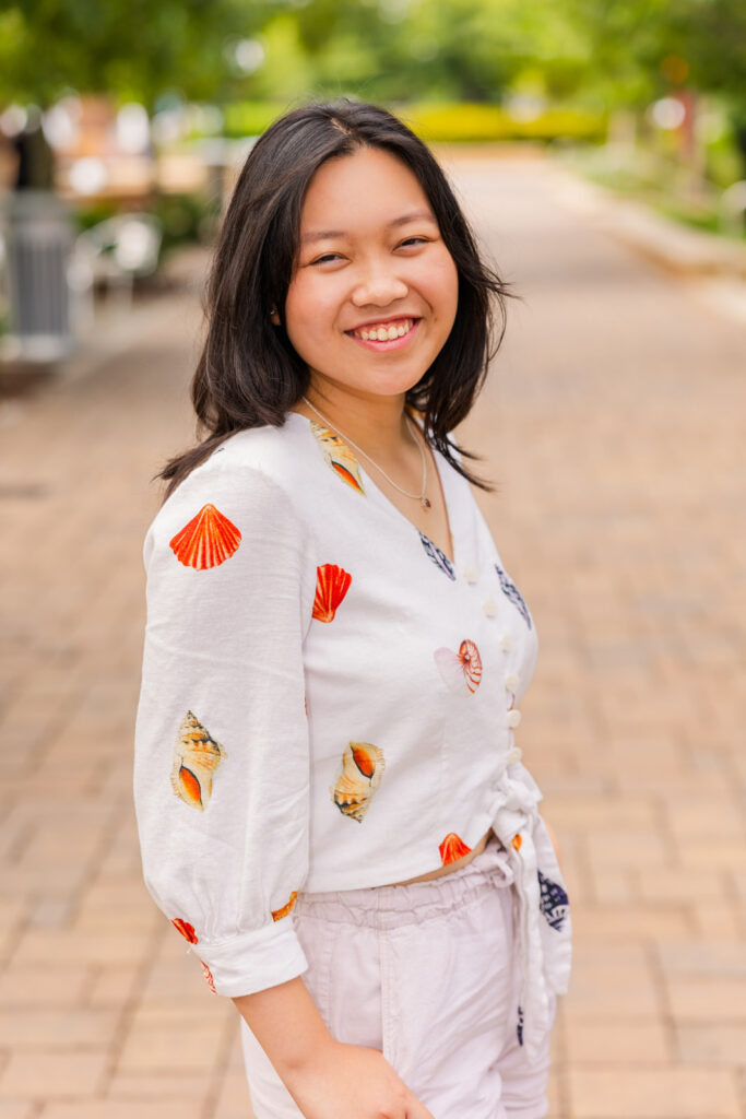 Senior girl wearing patterned summer shirt and shorts, standing in the street looking over her shoulder during portraits in Sandy Springs with Laure Photography.