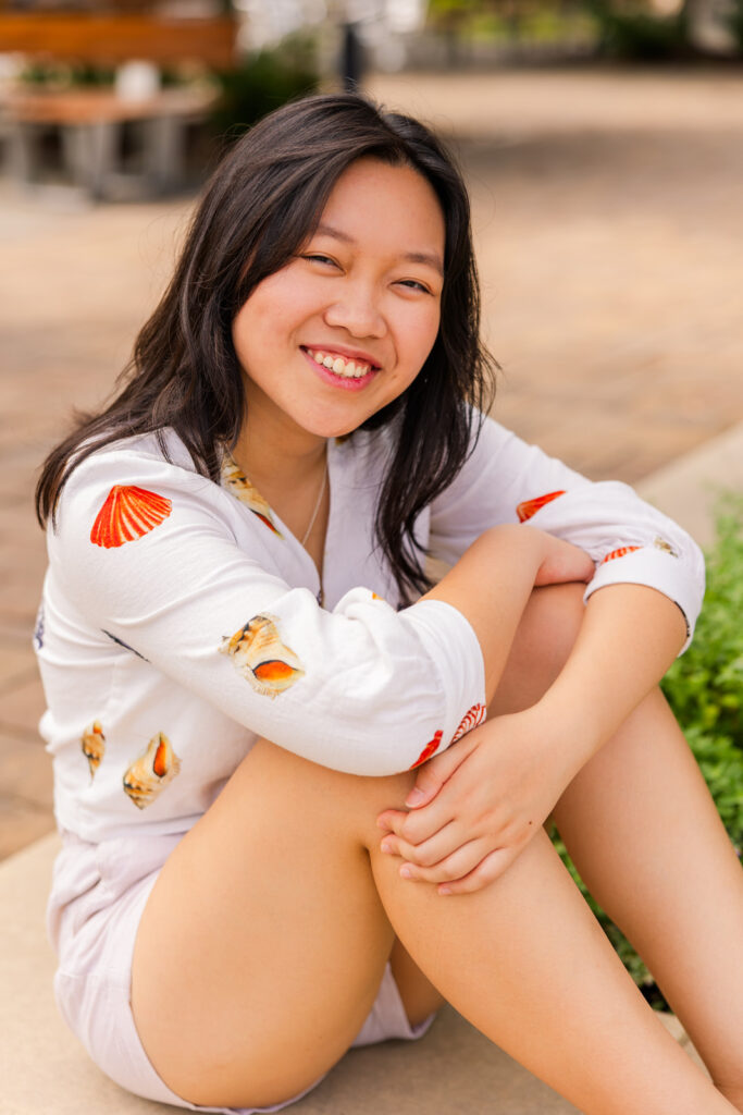 Senior girl sitting on the ground hugging her knees, wearing patterned summer shirt and shorts during her Atlanta senior portraits with Laure Photography.