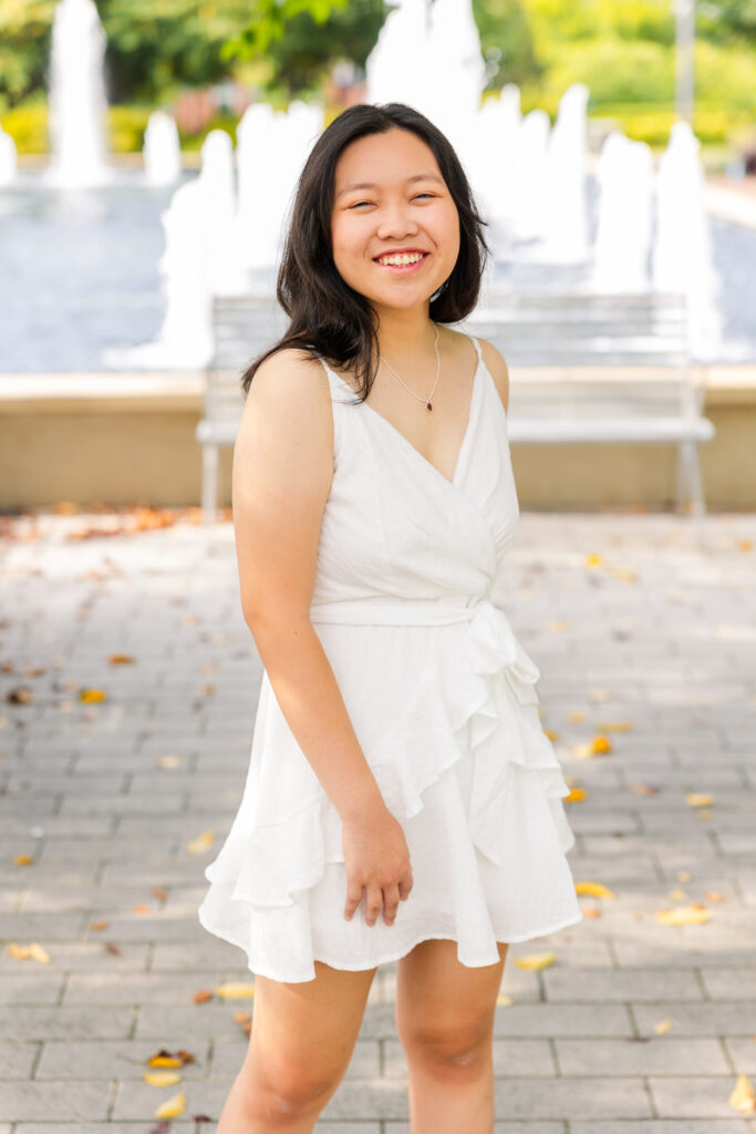 Senior girl twirling in front of a fountain, wearing a white summer dress during her joyful Sandy Springs senior session with Laure Photography.