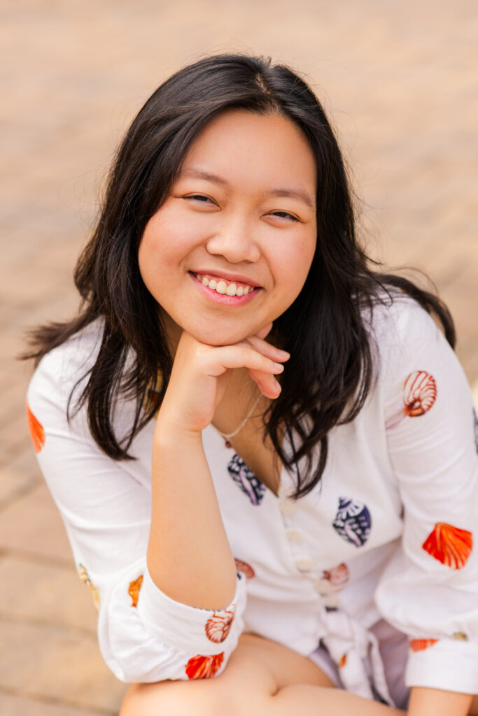 Senior girl sitting crisscross with hand under her chin, smiling softly during her Sandy Springs senior session with Laure Photography.