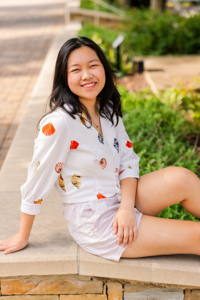 Senior girl sitting on a street wall with one knee up, wearing patterned shirt and shorts during her Atlanta senior portraits with Laure Photography.
