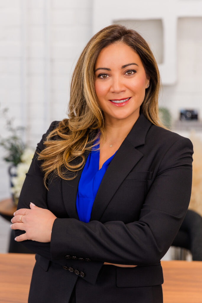 woman standing arms crossed against a desk with a lifestyle office background wearing corporate outfit blue top and and dark jacket during headshot photoshoot with Laure Photography