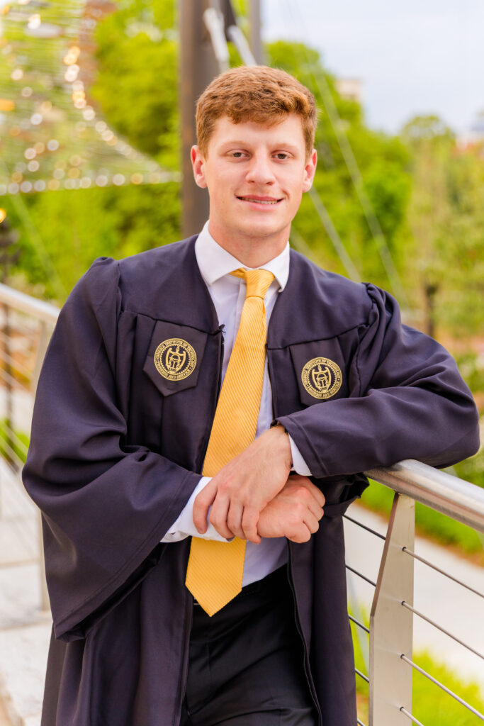 Half-body portrait of Jason facing the camera, elbow resting on a stair railway on campus during senior portraits
