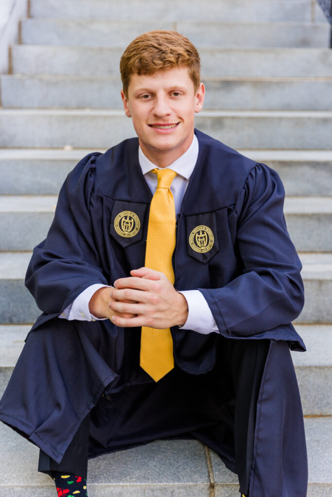 Jason sitting on campus stairs, facing the camera with hands together.