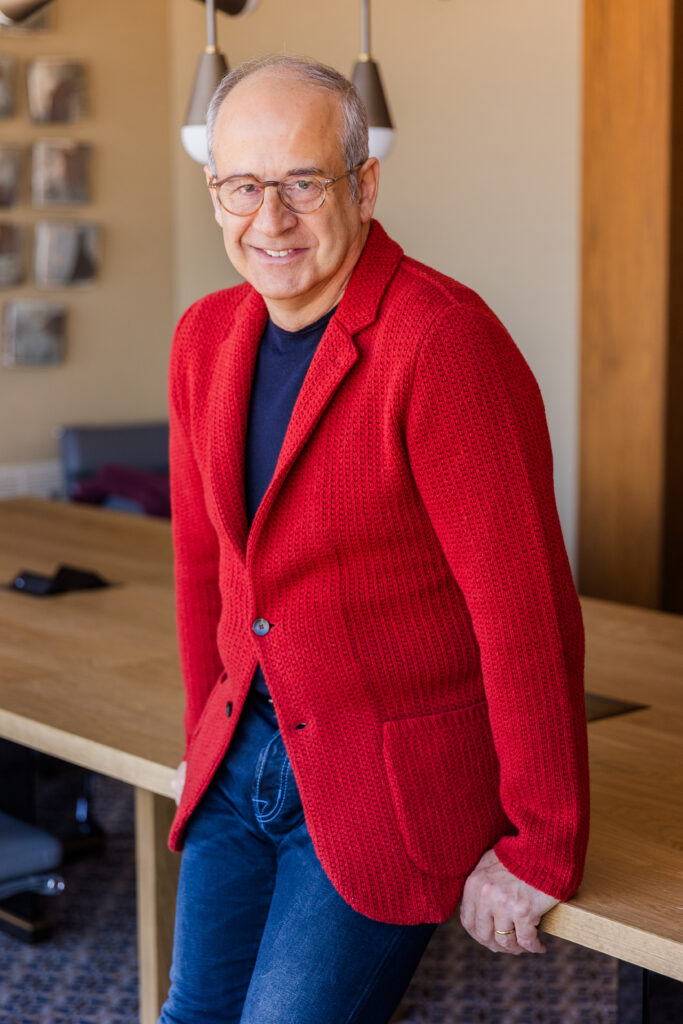 Ahmet Bozer leaning against a conference table, hands placed on either side, wearing a red casual jacket in Buckhead Atlanta