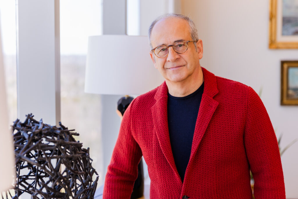 Headshot of Ahmet Bozer wearing a black t-shirt and red casual jacket, looking at the camera with office windows in the background